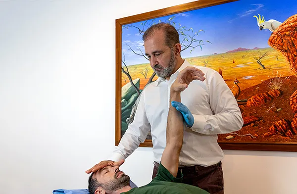 Dr Reza Samvat assessing a patient's arm and shoulder during a chiropractic session