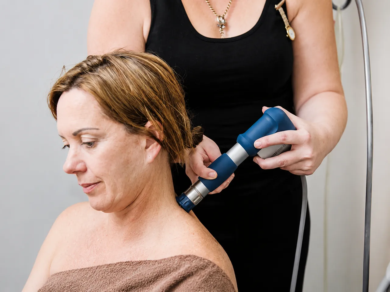 Practitioner applying shockwave therapy to a patient's neck and shoulder